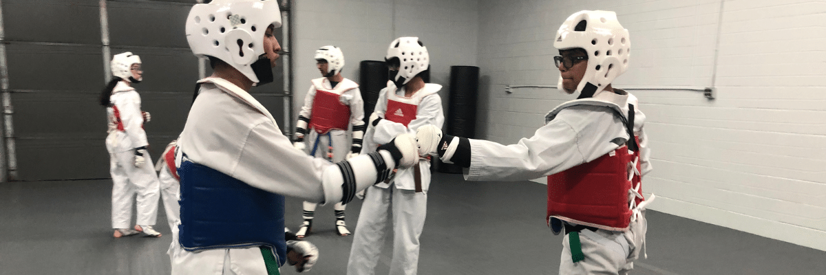 Two Akula Taekwondo students, dressed in protective gear, bump fists in preparation of sparring.