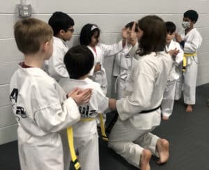 Group of children ages 5 and 6, dressed in karate uniforms, gather around their martial arts instructor at Akula Taekwondo.